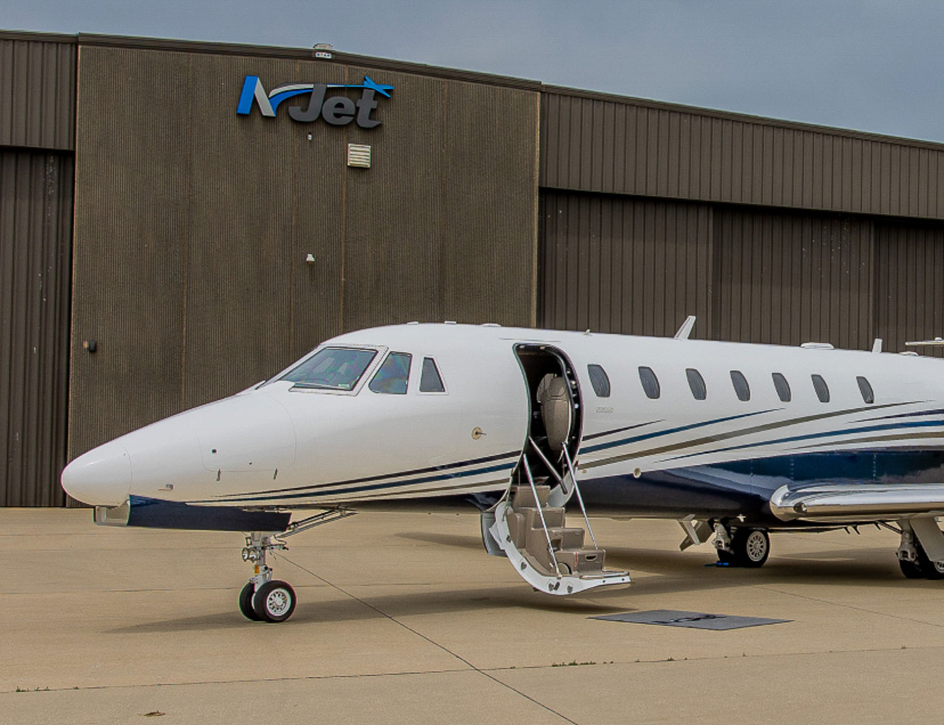 A private jet with an open door sitting outside a hangar